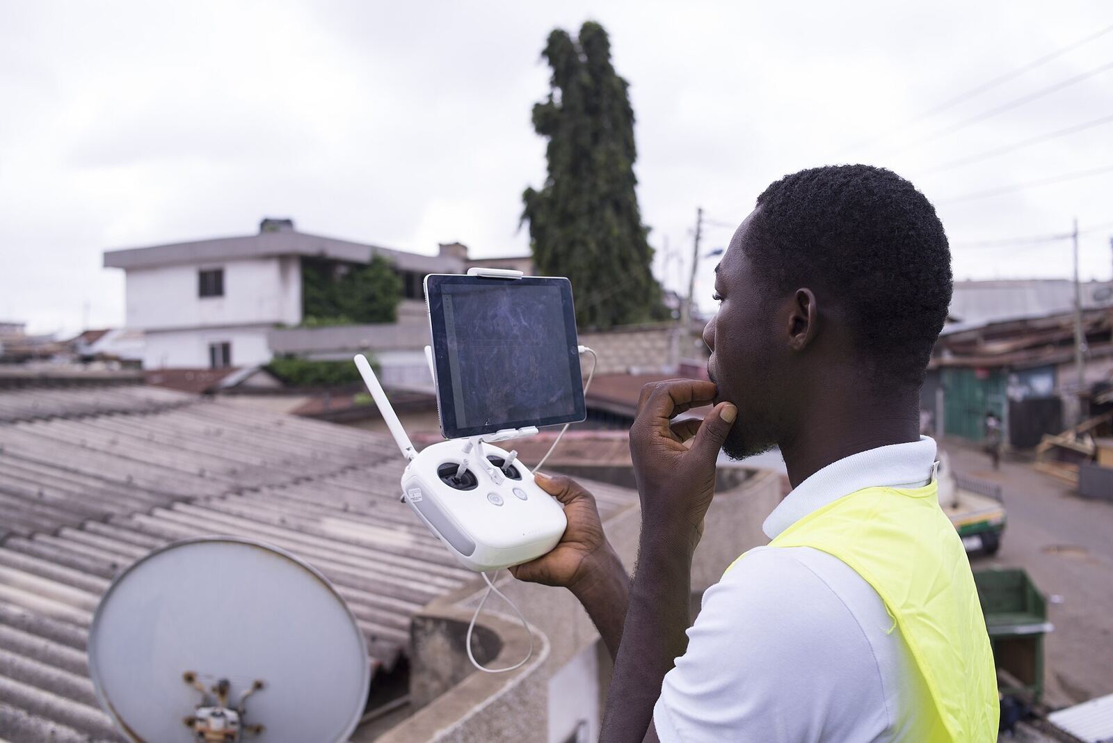A drone operator in a high-visibility vest looking up from his controller