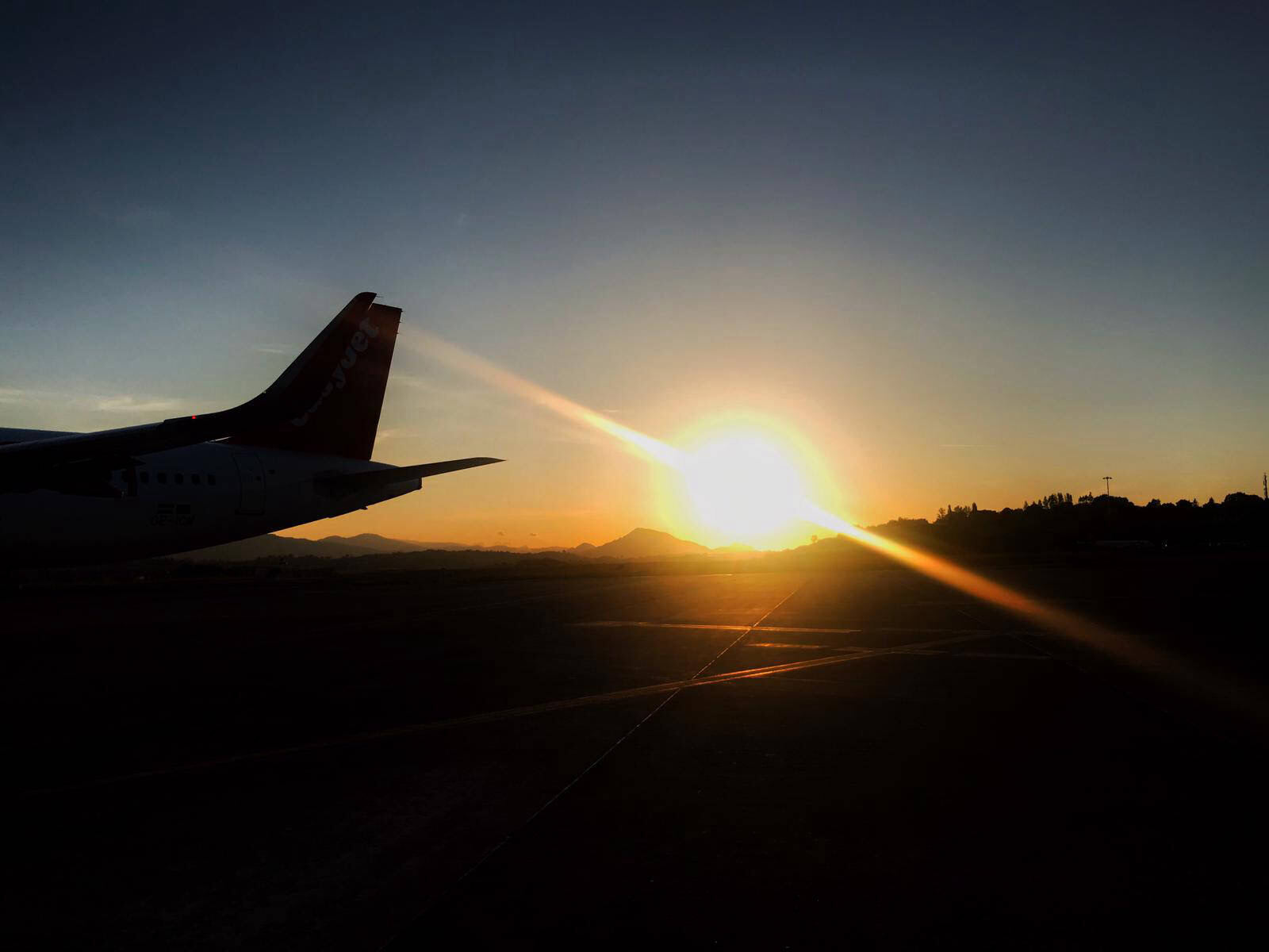 The tail of a parked aircraft silhouetted against the rising sun